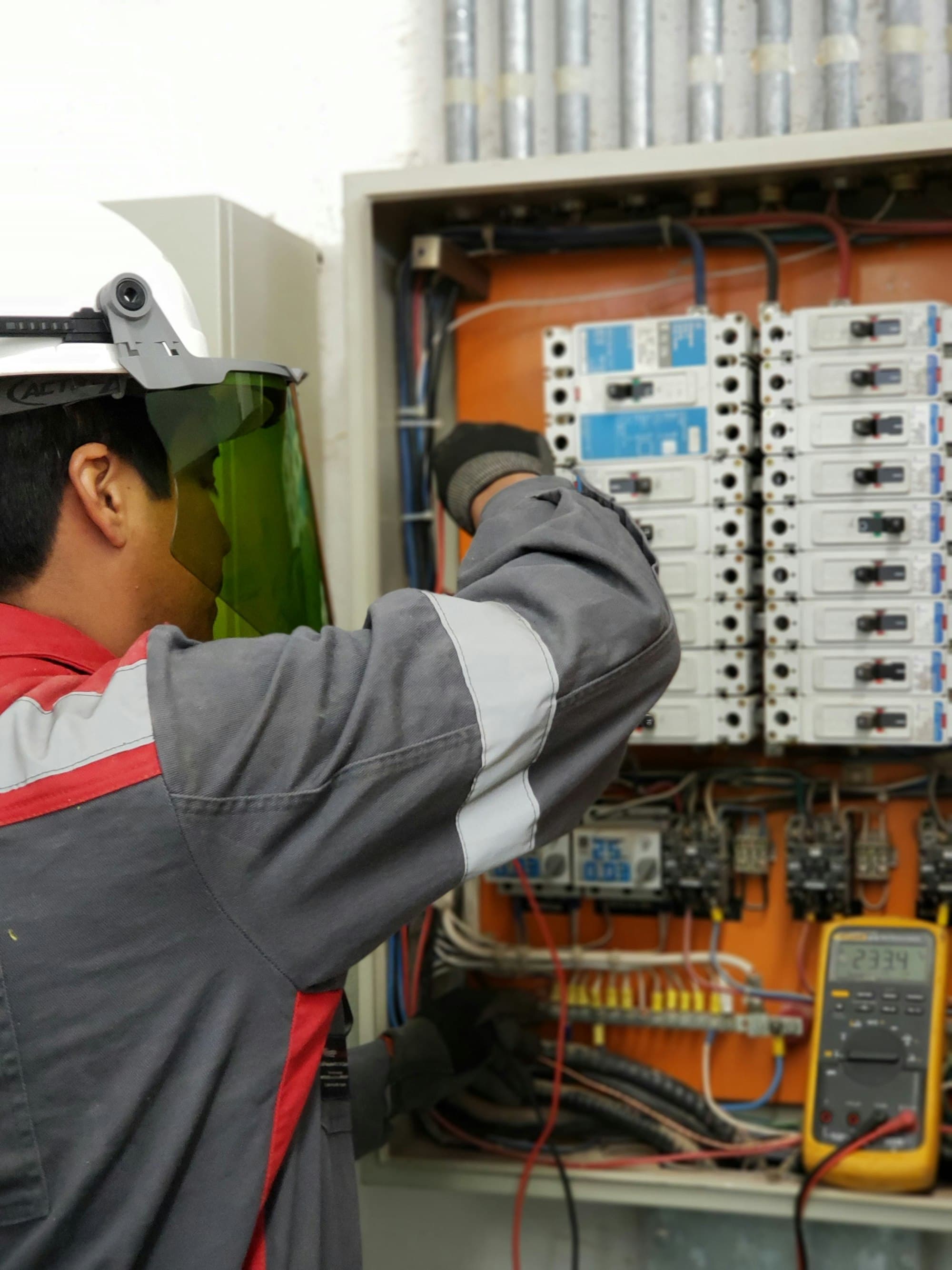 Technician in protective gear testing an electrical control panel